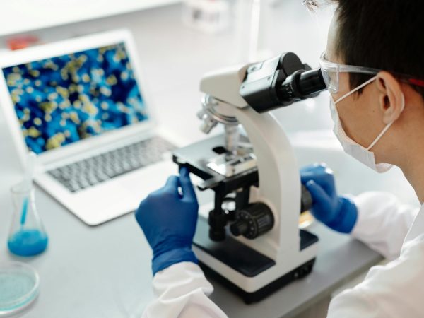 Scientist examining samples under a microscope in a lab with laptop display.